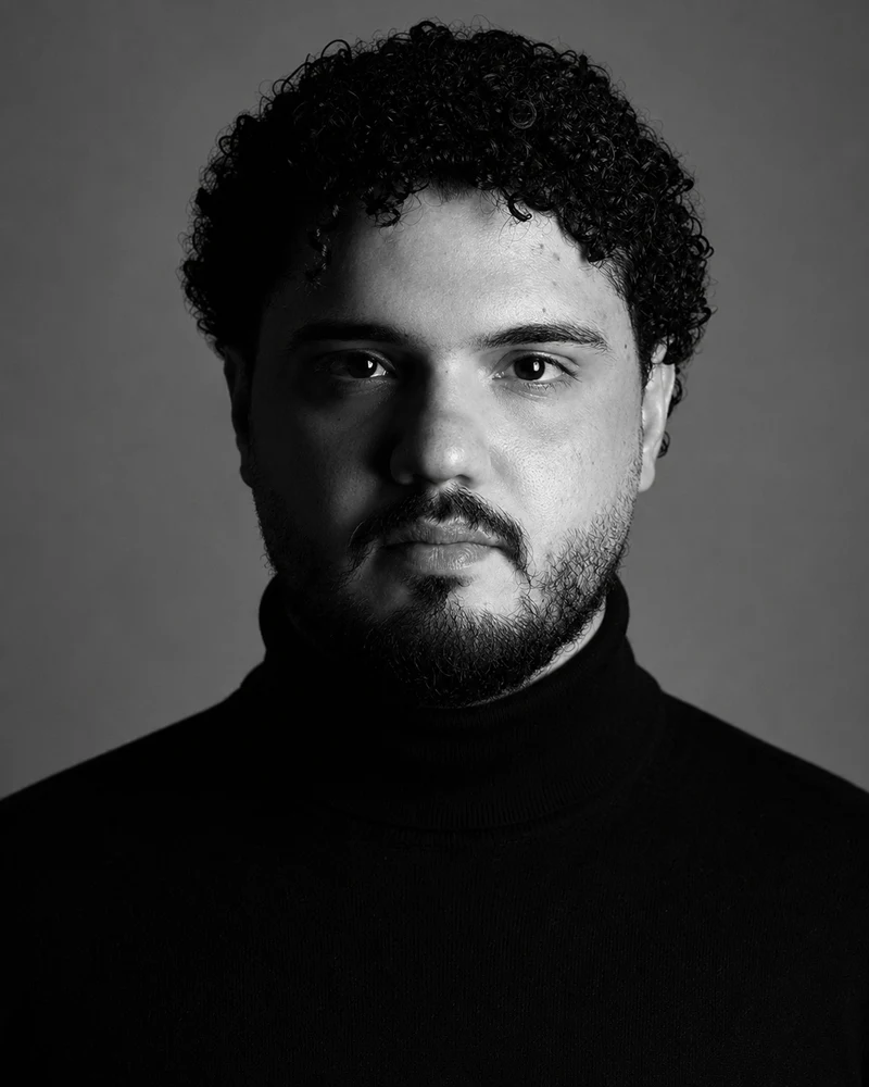 Black-and-white studio portrait of Omar Hagag in a black turtleneck, looking straight at the camera